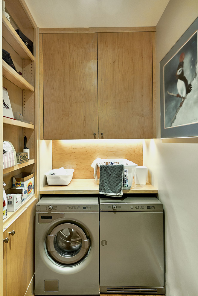 Diseño de cuarto de lavado en L actual con armarios con paneles lisos, puertas de armario de madera clara, encimera de madera, paredes blancas, lavadora y secadora juntas y encimeras beige