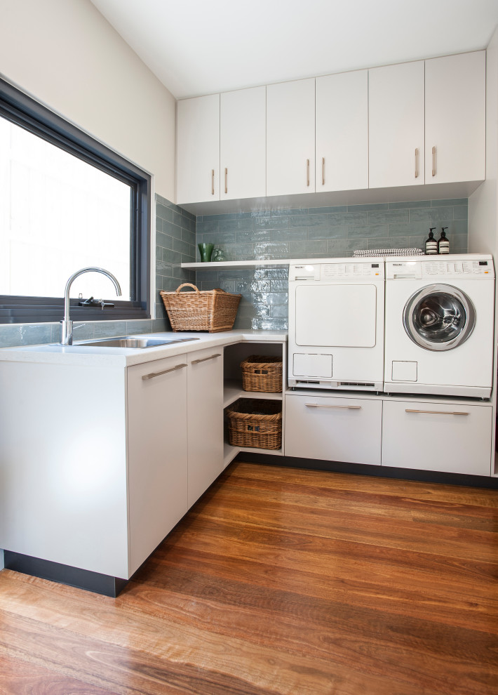 Inspiration for a large contemporary u-shaped medium tone wood floor and brown floor dedicated laundry room remodel in Melbourne with a single-bowl sink, white cabinets, laminate countertops, blue backsplash, subway tile backsplash, white walls, a side-by-side washer/dryer and gray countertops
