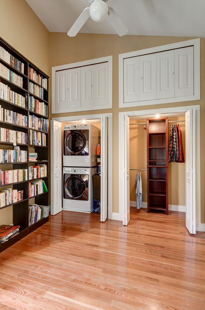 Imagen de armario lavadero tradicional renovado pequeño con paredes beige, suelo de madera en tonos medios y lavadora y secadora apiladas