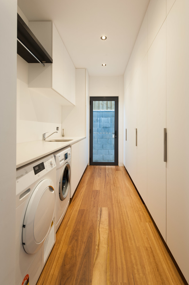 Photo of a large contemporary galley separated utility room in Brisbane with a submerged sink, flat-panel cabinets, white cabinets, laminate countertops, white walls, light hardwood flooring and a side by side washer and dryer.