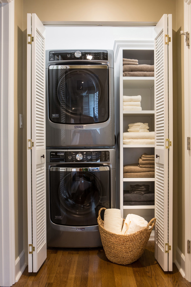 Foto de armario lavadero lineal clásico renovado pequeño con armarios abiertos, puertas de armario blancas, paredes blancas, suelo de madera en tonos medios y lavadora y secadora apiladas