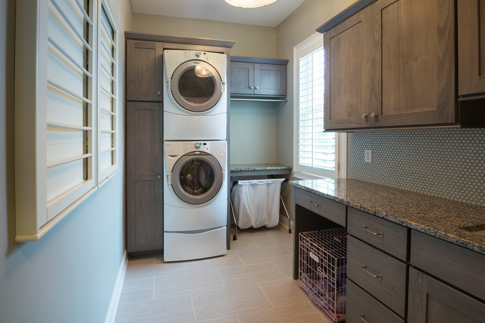 Design ideas for a medium sized traditional single-wall utility room in Indianapolis with a submerged sink, granite worktops, a stacked washer and dryer, flat-panel cabinets, ceramic flooring, dark wood cabinets and grey walls.
