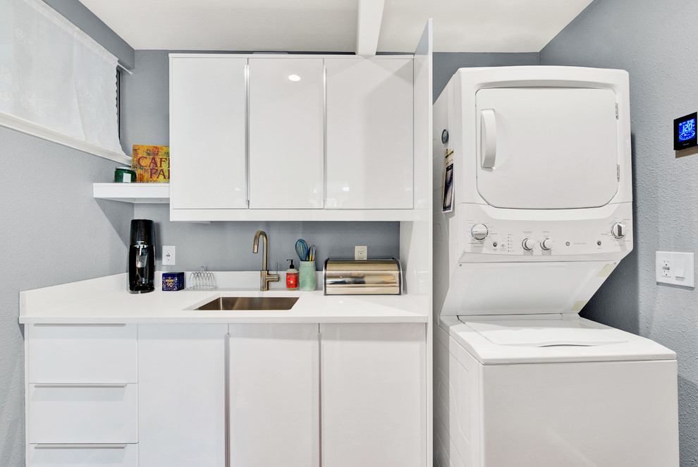 Imagen de lavadero multiusos moderno pequeño con fregadero bajoencimera, armarios con paneles lisos, puertas de armario blancas, encimera de cuarzo compacto y lavadora y secadora apiladas