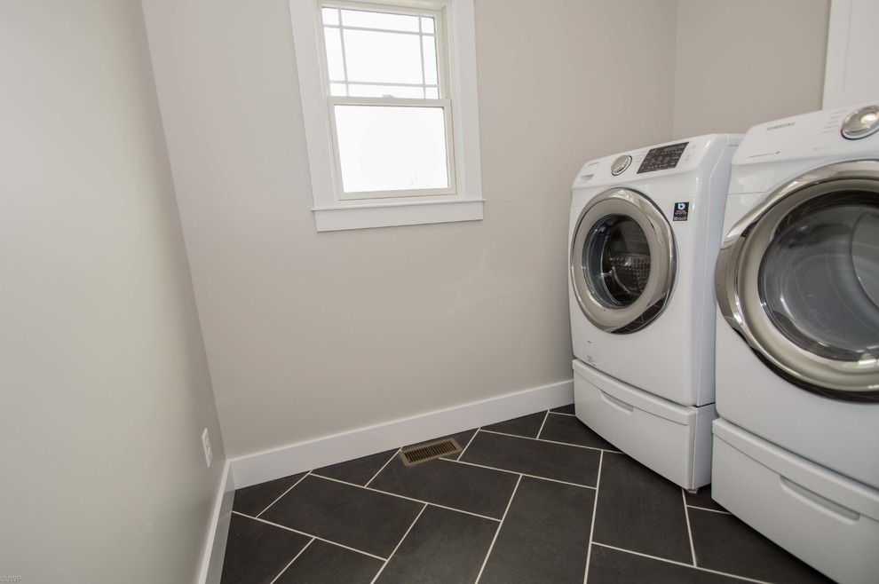 Einzeilige, Mittelgroße Klassische Waschküche mit grauer Wandfarbe, Porzellan-Bodenfliesen, Waschmaschine und Trockner nebeneinander und schwarzem Boden in Chicago