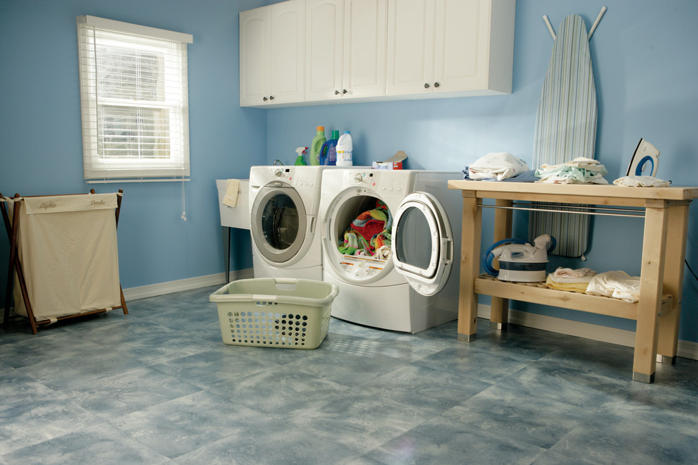 Inredning av en modern linjär tvättstuga, med en allbänk, luckor med upphöjd panel, vita skåp, blå väggar, vinylgolv och en tvättmaskin och torktumlare bredvid varandra