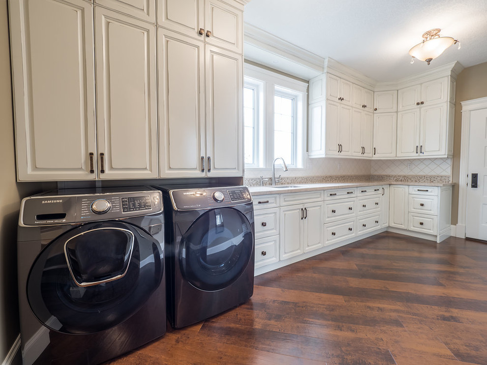 Example of a large classic l-shaped vinyl floor and multicolored floor dedicated laundry room design in Edmonton with a drop-in sink, raised-panel cabinets, white cabinets, granite countertops, beige walls and a side-by-side washer/dryer