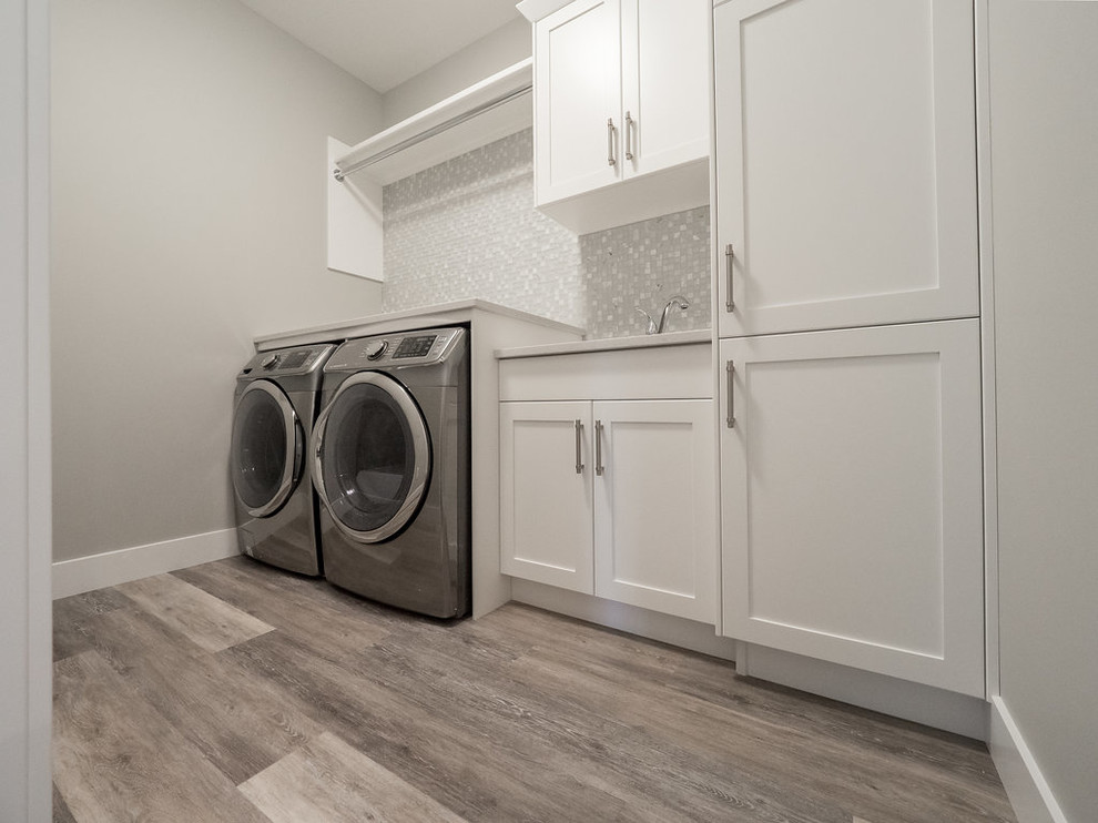 Large elegant single-wall vinyl floor and multicolored floor dedicated laundry room photo in Edmonton with a double-bowl sink, recessed-panel cabinets, white cabinets, solid surface countertops, gray walls and a side-by-side washer/dryer
