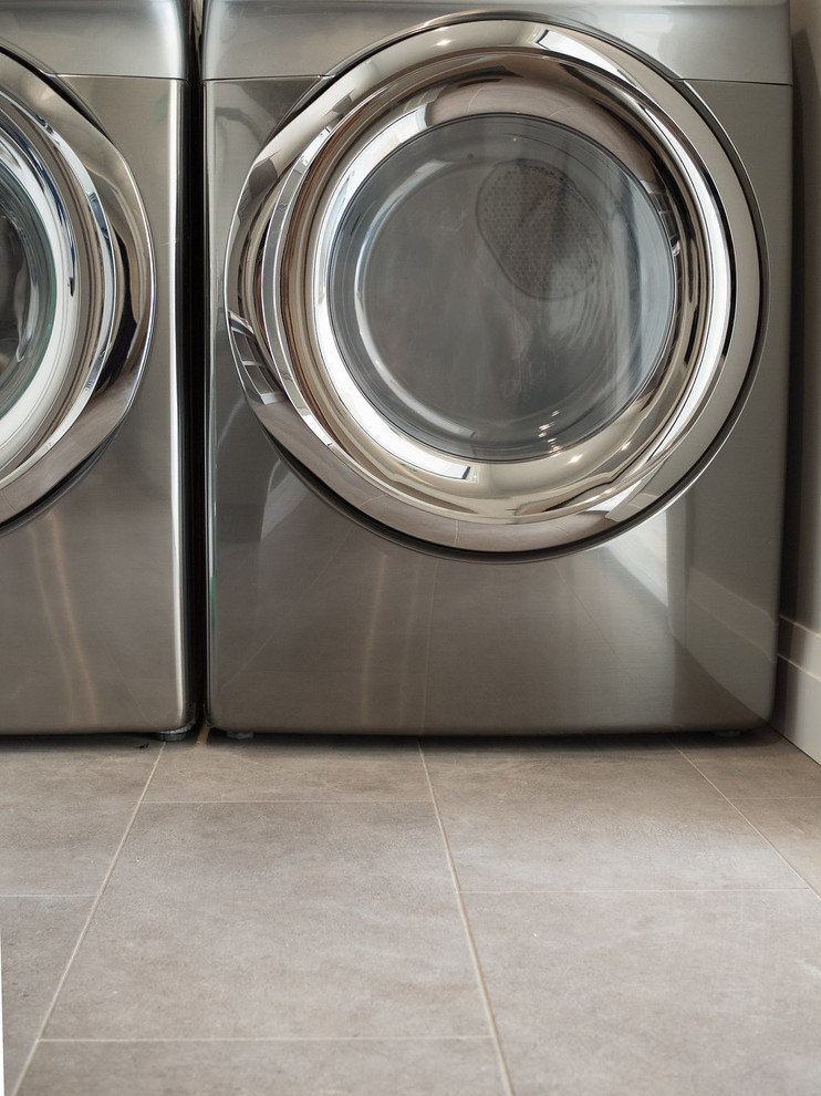 Foto på en mellanstor funkis l-formad tvättstuga enbart för tvätt, med grå väggar, vinylgolv, en tvättmaskin och torktumlare bredvid varandra och grått golv