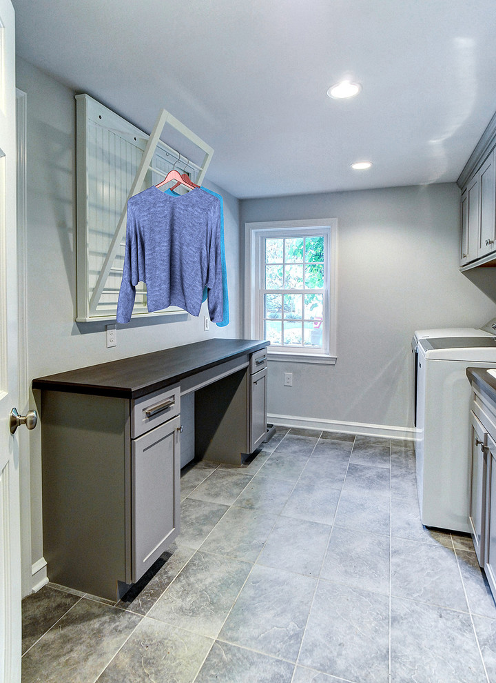 Klassisk inredning av en bruna brunt tvättstuga, med en allbänk, luckor med infälld panel, grå skåp, laminatbänkskiva, grå väggar, klinkergolv i porslin, en tvättmaskin och torktumlare bredvid varandra och grått golv