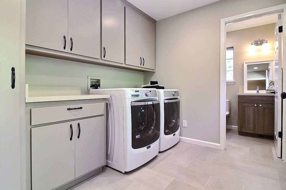 Example of a mid-sized classic single-wall travertine floor utility room design in San Francisco with flat-panel cabinets, gray cabinets, solid surface countertops, beige walls and a side-by-side washer/dryer