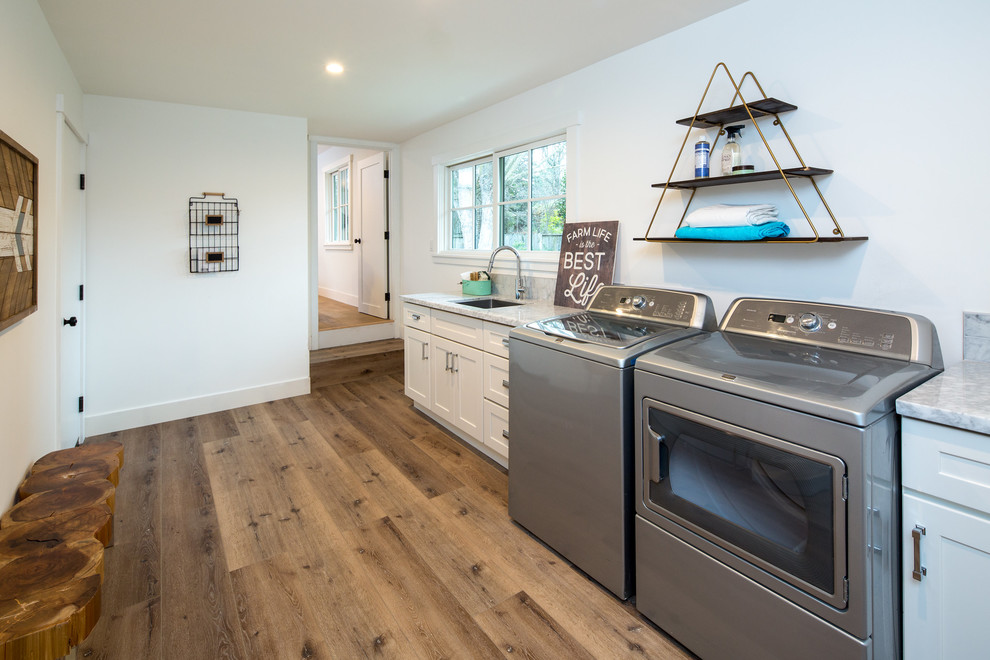 Large farmhouse single-wall utility room in San Francisco with a submerged sink, shaker cabinets, white cabinets, marble worktops, white walls, medium hardwood flooring and a side by side washer and dryer.