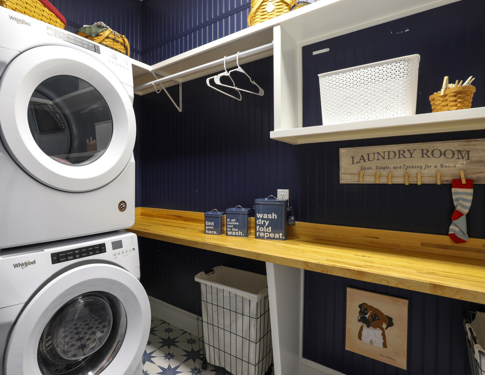 ジャクソンビルにあるお手頃価格の小さなカントリー風のおしゃれな洗濯室 (シェーカースタイル扉のキャビネット、白いキャビネット、木材カウンター、青いキッチンパネル、塗装板のキッチンパネル、青い壁、磁器タイルの床、上下配置の洗濯機・乾燥機、青い床、白いキッチンカウンター、パネル壁) の写真