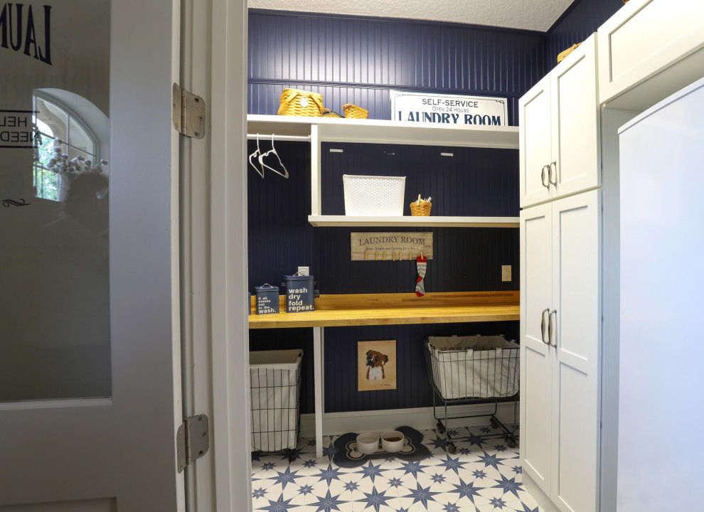 Bild på en liten lantlig vita vitt tvättstuga enbart för tvätt, med skåp i shakerstil, vita skåp, träbänkskiva, blått stänkskydd, blå väggar, klinkergolv i porslin, en tvättpelare och blått golv