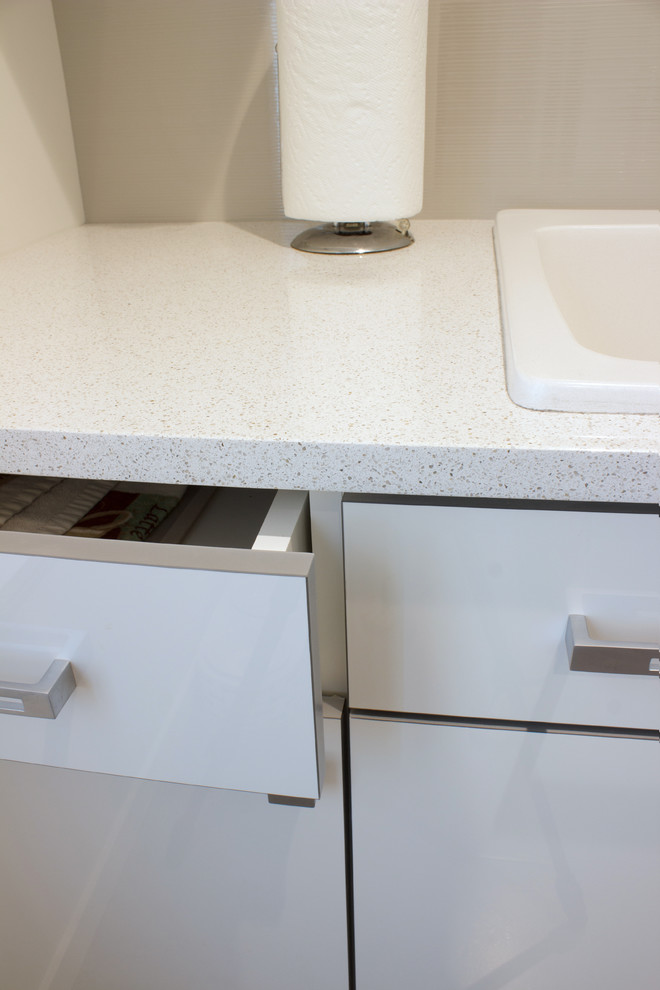 This is an example of a small contemporary galley separated utility room in New York with a built-in sink, flat-panel cabinets, white cabinets, granite worktops, grey walls, porcelain flooring and a side by side washer and dryer.