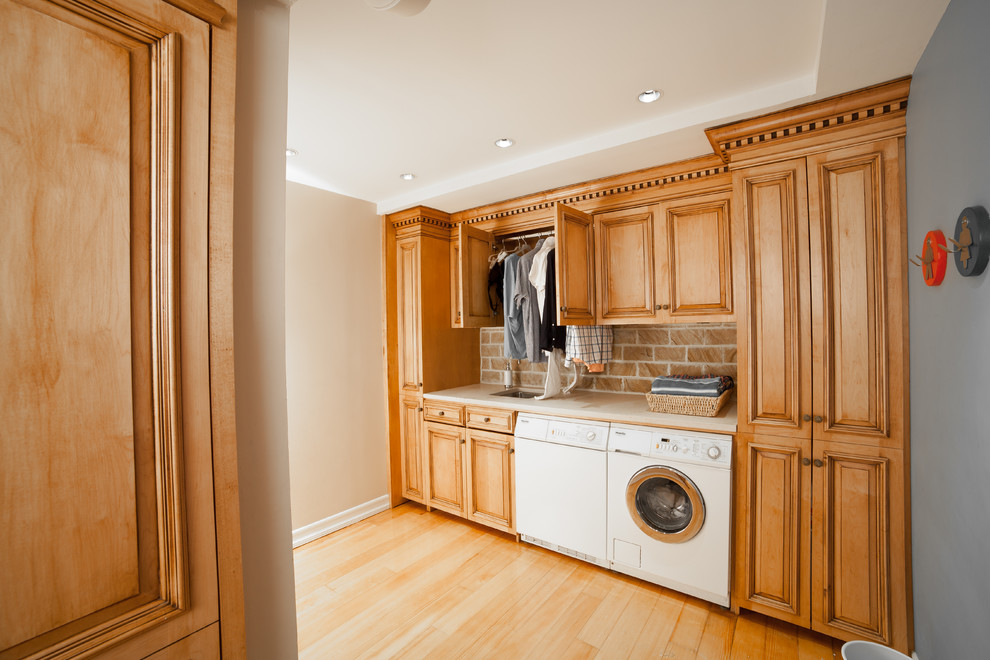 Small elegant single-wall light wood floor and brown floor utility room photo in New York with a single-bowl sink, raised-panel cabinets, a side-by-side washer/dryer, medium tone wood cabinets, granite countertops, multicolored walls and beige countertops