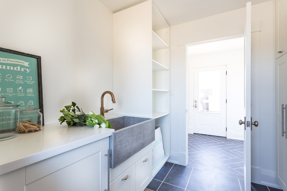 Photo of a large coastal galley separated utility room in Toronto with a belfast sink, shaker cabinets, white cabinets, engineered stone countertops, white walls, slate flooring and grey floors.