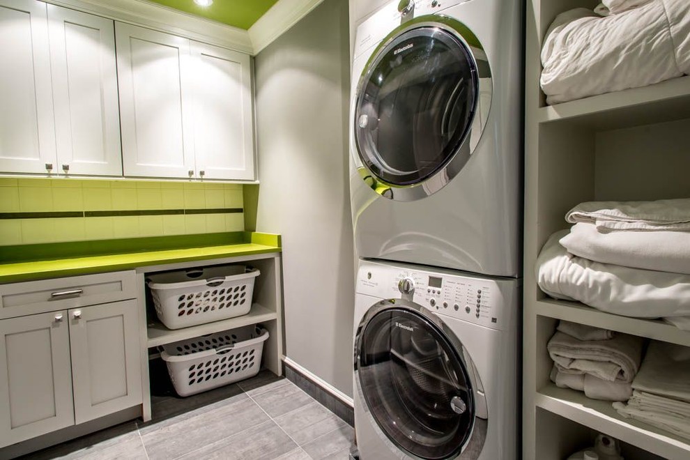 Example of a classic l-shaped ceramic tile laundry room design in DC Metro with shaker cabinets, white cabinets, a stacked washer/dryer, solid surface countertops and green countertops