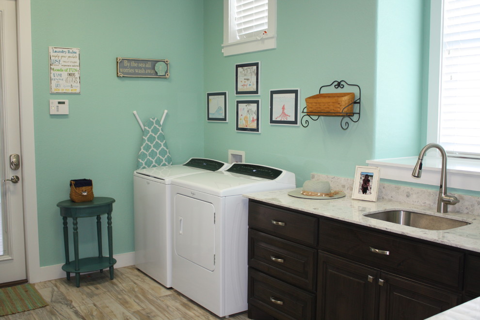 This is an example of a large nautical separated utility room in Houston with a submerged sink, raised-panel cabinets, dark wood cabinets, composite countertops, green walls, porcelain flooring and a side by side washer and dryer.