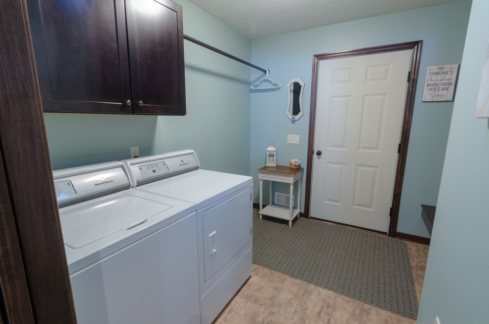 Klassische Waschküche mit braunen Schränken, blauer Wandfarbe, Keramikboden, Waschmaschine und Trockner nebeneinander und grauem Boden in Milwaukee