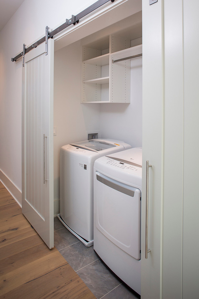 Ejemplo de armario lavadero lineal actual pequeño con puertas de armario blancas, paredes blancas, suelo de baldosas de porcelana y lavadora y secadora juntas