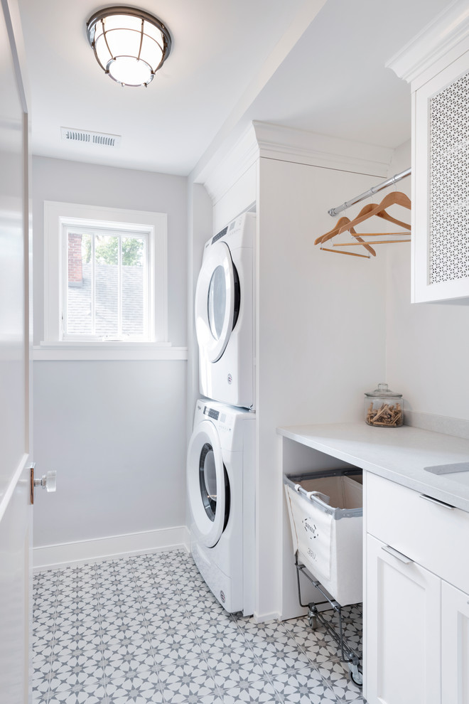 Inspiration for a small transitional single-wall ceramic tile and multicolored floor dedicated laundry room remodel in Minneapolis with a stacked washer/dryer, an undermount sink, shaker cabinets, white cabinets, gray walls and white countertops