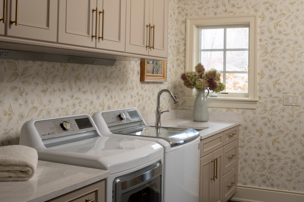 Example of a mid-sized classic single-wall wallpaper dedicated laundry room design in Minneapolis with an undermount sink, recessed-panel cabinets, beige cabinets, quartz countertops, beige backsplash, quartz backsplash, multicolored walls, a side-by-side washer/dryer and beige countertops