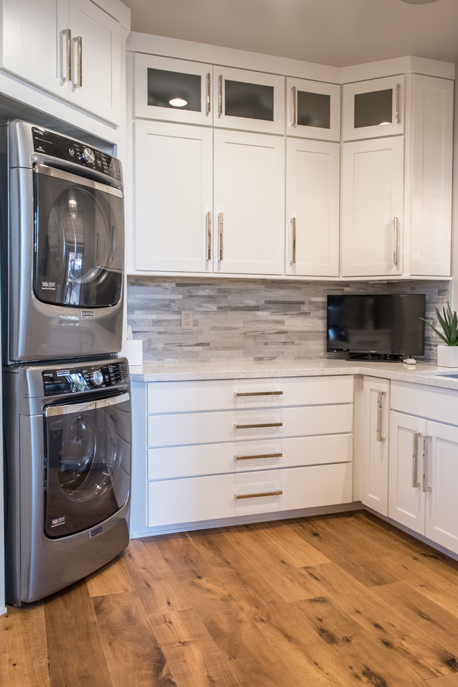 Rustic u-shaped utility room in Phoenix with a submerged sink, shaker cabinets, white cabinets, black walls, medium hardwood flooring, a stacked washer and dryer, brown floors and white worktops.