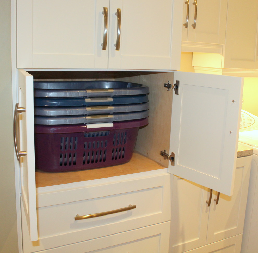 Klassisk inredning av en tvättstuga, med skåp i shakerstil, vita skåp och en tvättmaskin och torktumlare bredvid varandra