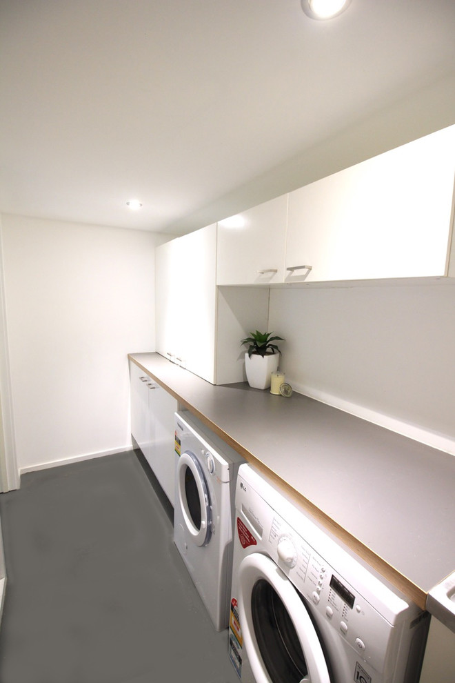 Immagine di una sala lavanderia minimal di medie dimensioni con ante bianche, pareti bianche, pavimento in cemento e lavatrice e asciugatrice affiancate