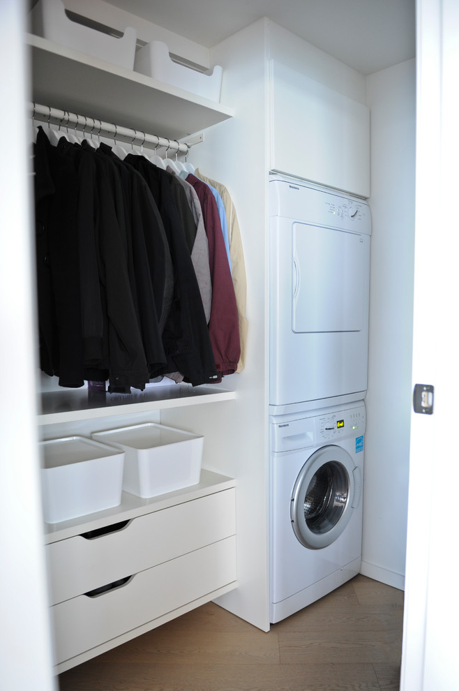 Immagine di una piccola lavanderia multiuso moderna con ante lisce, ante bianche, top in laminato, pareti bianche, parquet chiaro e lavatrice e asciugatrice a colonna