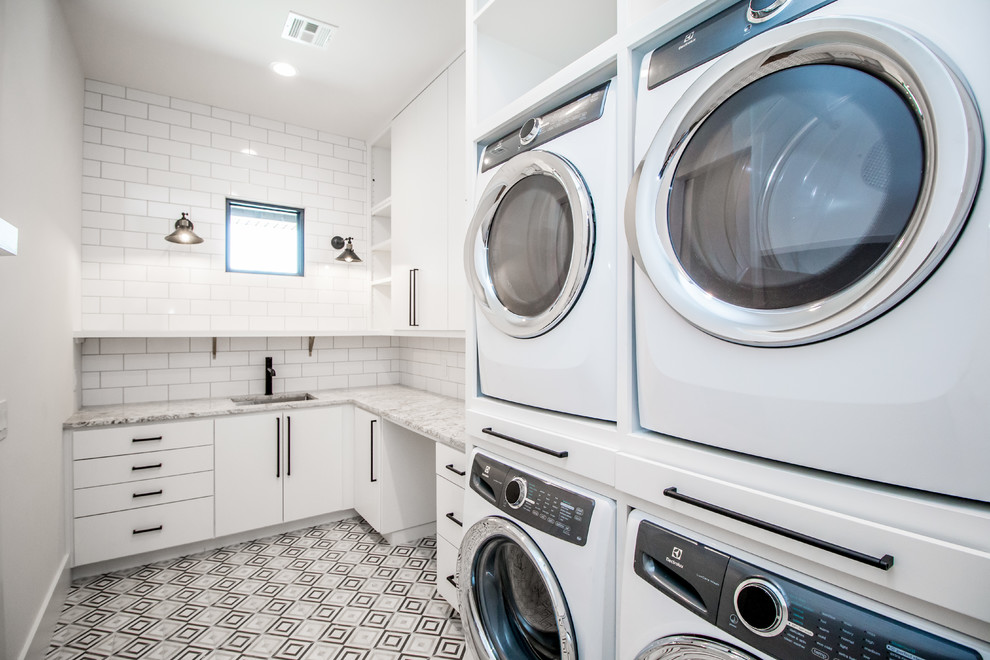 This is an example of a medium sized contemporary l-shaped utility room in Other with a submerged sink, multi-coloured floors, flat-panel cabinets, white cabinets, granite worktops, white walls and a stacked washer and dryer.