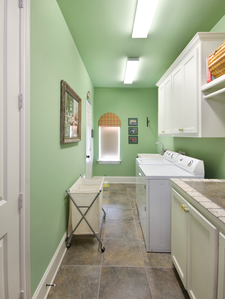 ニューオリンズにある高級な中くらいなトラディショナルスタイルのおしゃれな洗濯室 (I型、落し込みパネル扉のキャビネット、白いキャビネット、タイルカウンター、緑の壁、左右配置の洗濯機・乾燥機) の写真