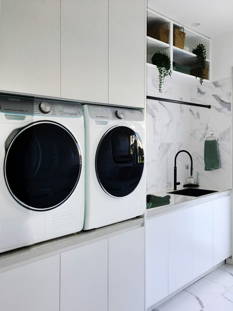 Bild på en mellanstor funkis vita linjär vitt tvättstuga enbart för tvätt, med en nedsänkt diskho, släta luckor, vita skåp, bänkskiva i kvarts, vita väggar, marmorgolv, en tvättmaskin och torktumlare bredvid varandra och vitt golv