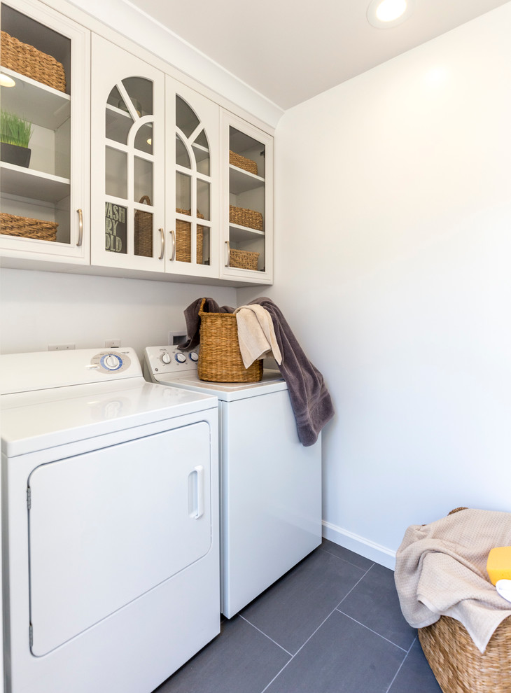 ロサンゼルスにある中くらいなトランジショナルスタイルのおしゃれな洗濯室 (I型、ガラス扉のキャビネット、白いキャビネット、白い壁、磁器タイルの床、左右配置の洗濯機・乾燥機、グレーの床) の写真