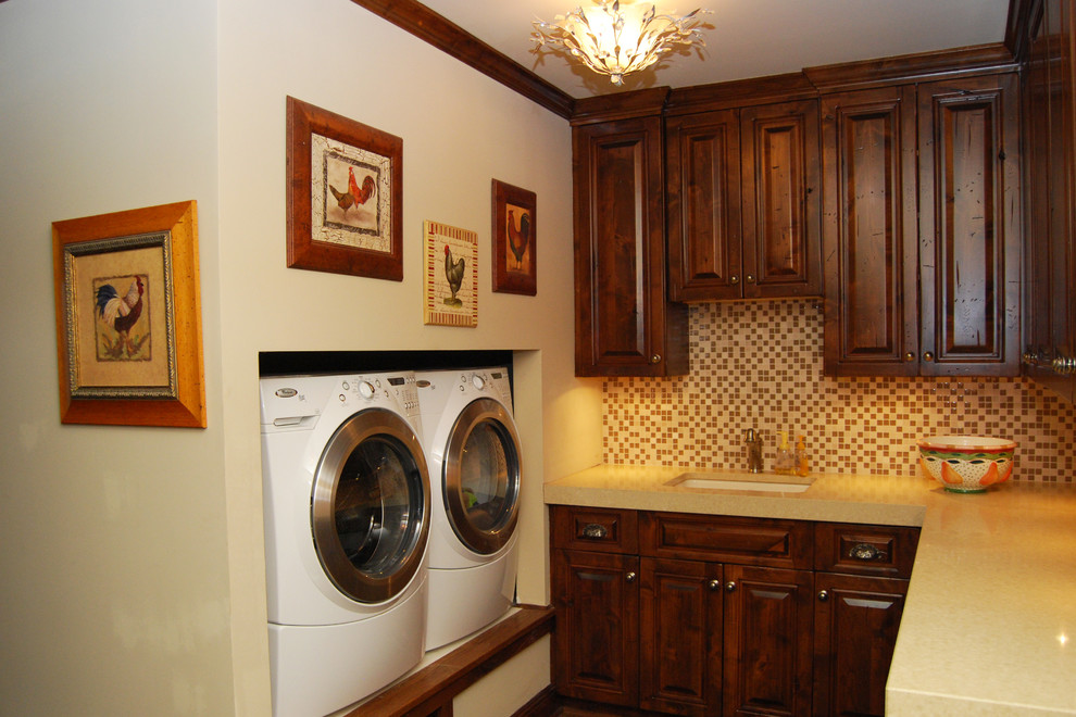 Immagine di una lavanderia rustica di medie dimensioni con lavello sottopiano, ante con bugna sagomata, ante in legno bruno, top in quarzo composito, pareti bianche e lavatrice e asciugatrice affiancate