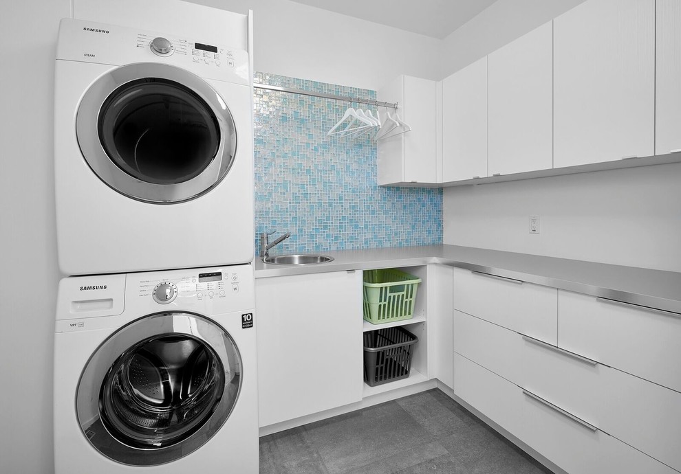 Inspiration för en mellanstor vintage l-formad tvättstuga enbart för tvätt, med en nedsänkt diskho, släta luckor, vita skåp, bänkskiva i rostfritt stål, vita väggar, skiffergolv, en tvättpelare och grått golv