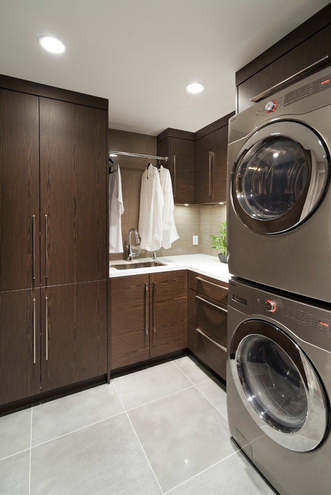 Imagen de lavadero actual con puertas de armario de madera en tonos medios, lavadora y secadora apiladas y encimeras blancas