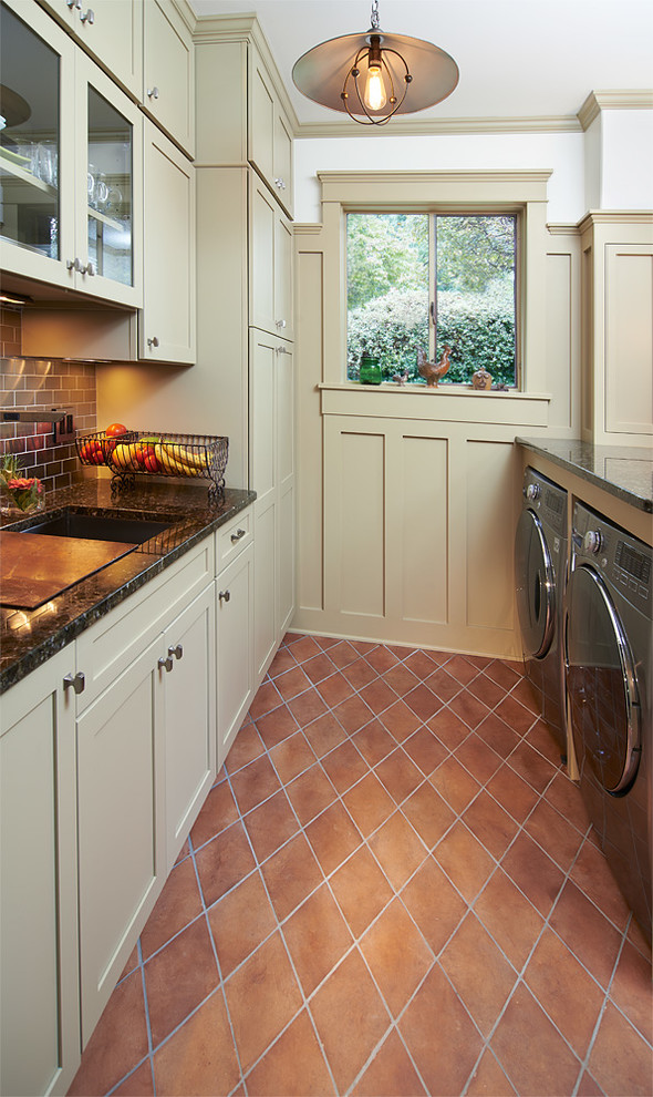 Exempel på ett mellanstort amerikanskt parallellt grovkök, med luckor med infälld panel, beige skåp, vita väggar, klinkergolv i keramik, en tvättmaskin och torktumlare bredvid varandra, granitbänkskiva och orange golv