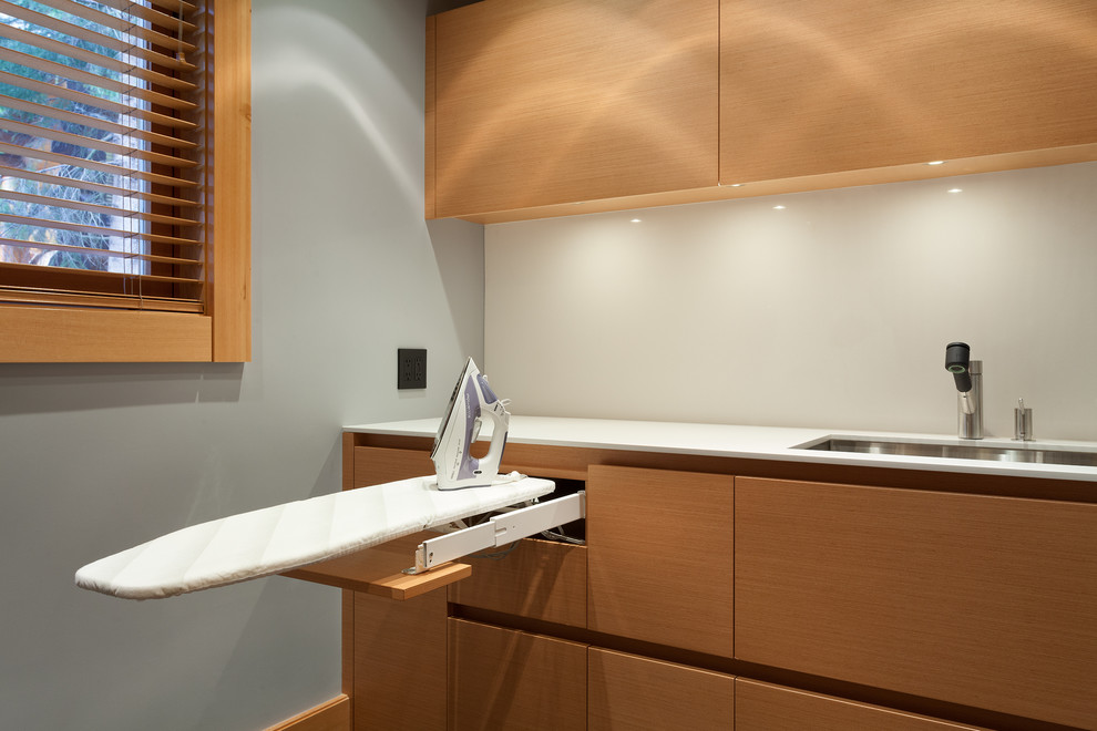 Foto di una piccola sala lavanderia minimalista con lavello sottopiano, ante lisce, ante in legno chiaro, top in superficie solida, pareti grigie, pavimento in cemento, pavimento grigio e top bianco