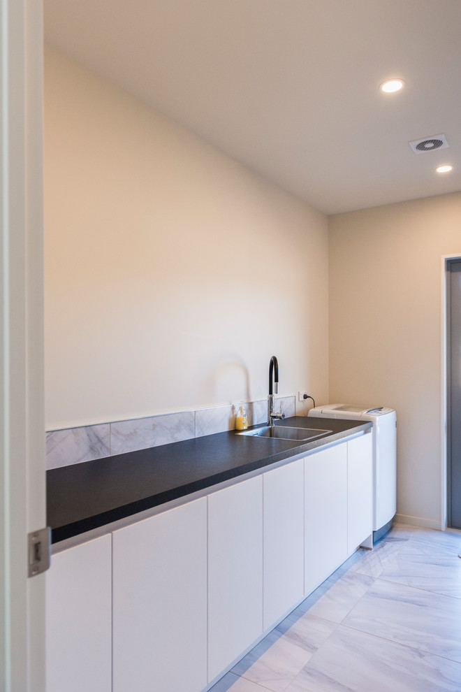 Dedicated laundry room - mid-sized contemporary single-wall linoleum floor and white floor dedicated laundry room idea in Christchurch with a drop-in sink, flat-panel cabinets, white cabinets, laminate countertops and white walls