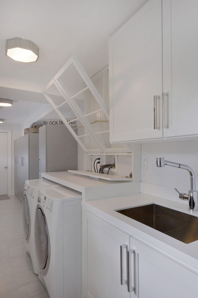 Design ideas for a large modern single-wall separated utility room in New York with a submerged sink, recessed-panel cabinets, white cabinets, composite countertops, white walls, porcelain flooring and a side by side washer and dryer.