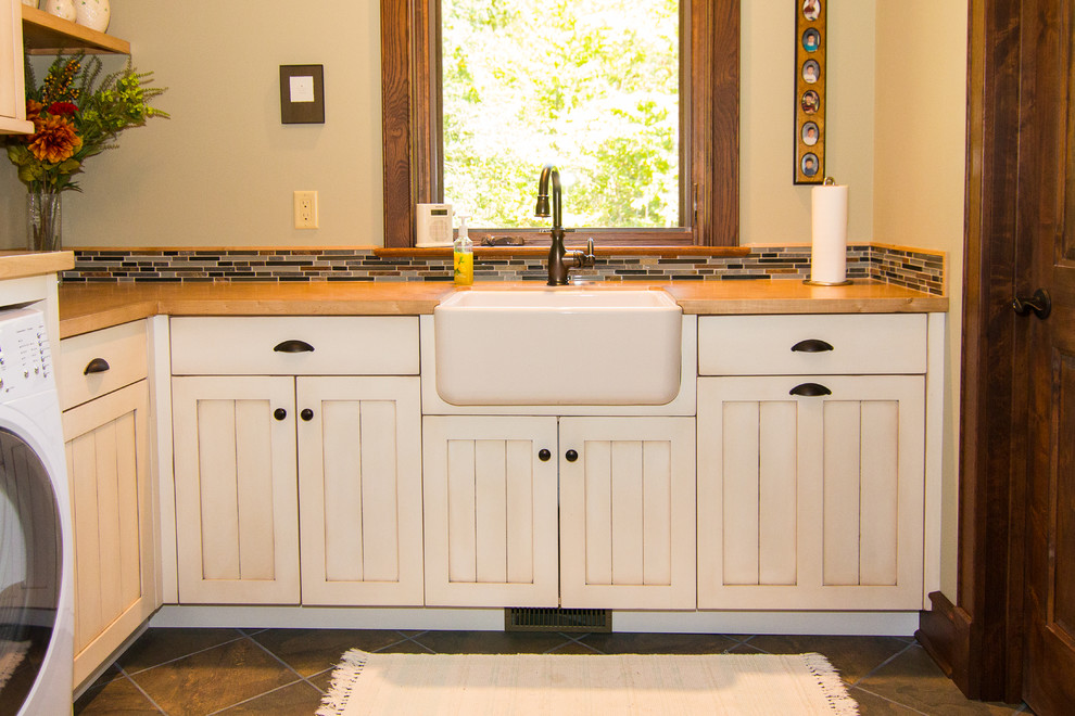 Inspiration for a large country laundry room remodel in Other with a farmhouse sink, recessed-panel cabinets, wood countertops, beige walls, a side-by-side washer/dryer and white cabinets