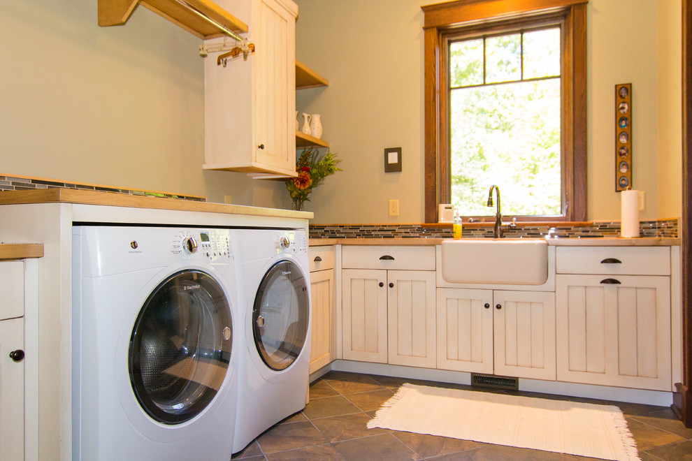 Inredning av en lantlig stor tvättstuga, med en rustik diskho, luckor med infälld panel, träbänkskiva, beige väggar, en tvättmaskin och torktumlare bredvid varandra och vita skåp