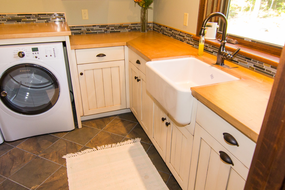 Laundry room - large farmhouse laundry room idea in Other with a farmhouse sink, recessed-panel cabinets, wood countertops, beige walls, a side-by-side washer/dryer and white cabinets