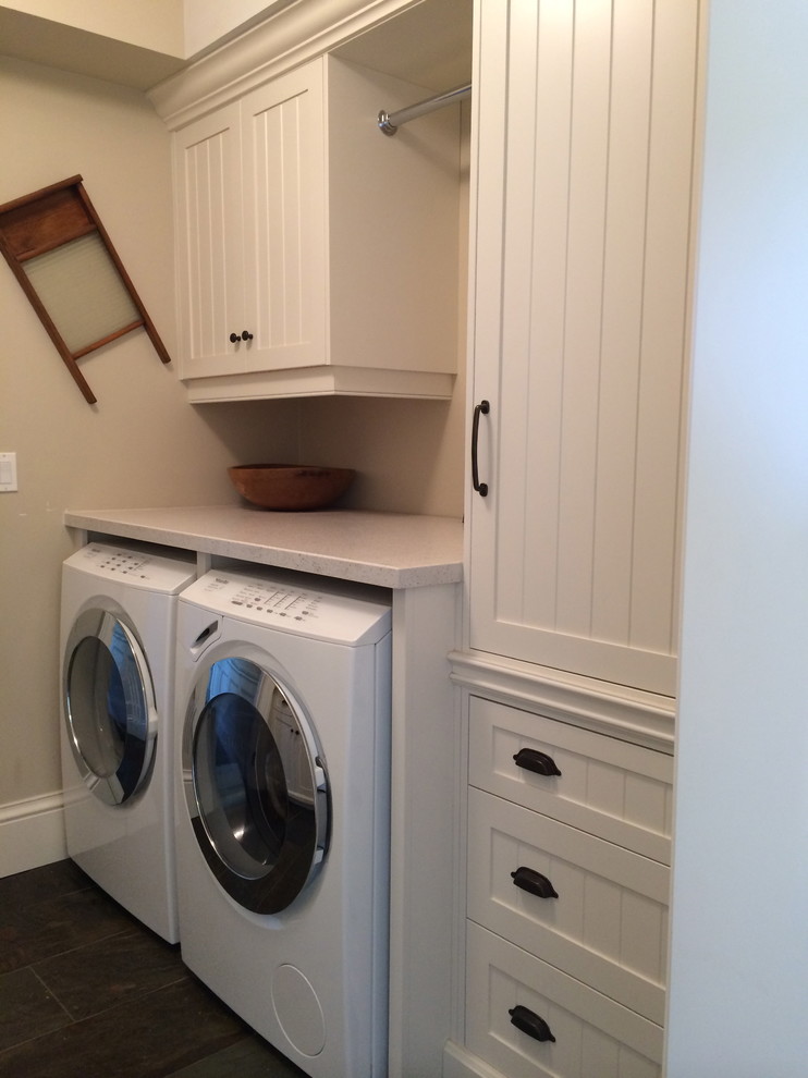 Klassisk inredning av en parallell tvättstuga enbart för tvätt, med en undermonterad diskho, släta luckor, vita skåp, beige väggar, skiffergolv och en tvättmaskin och torktumlare bredvid varandra