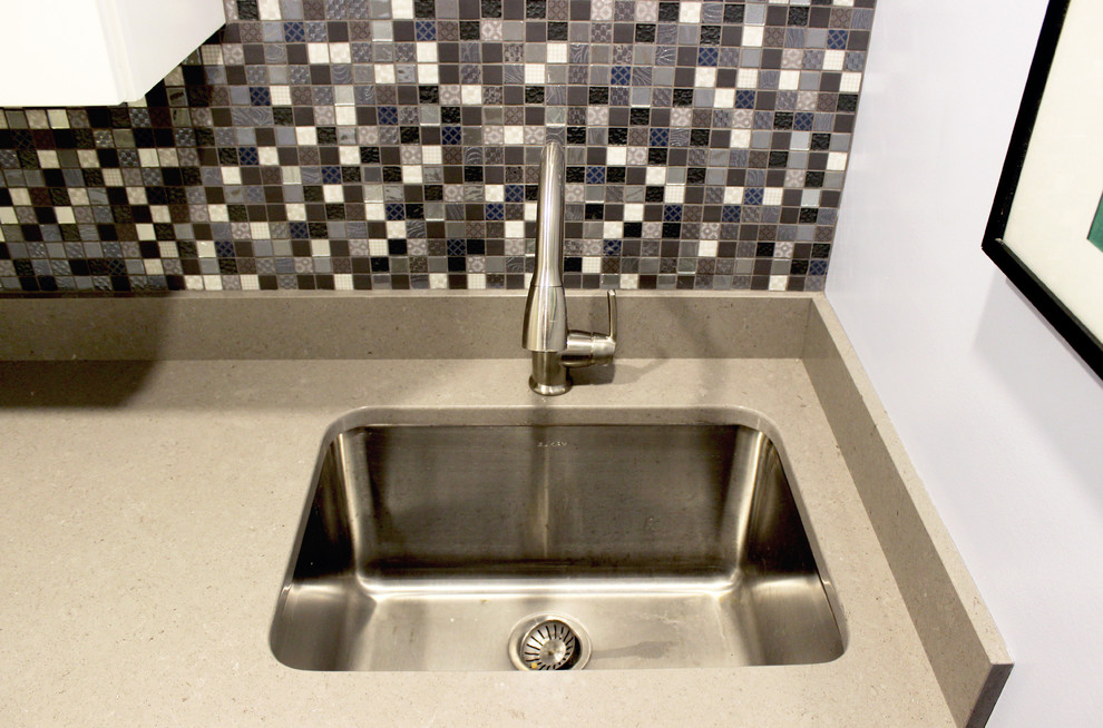 Exempel på en liten klassisk beige parallell beige tvättstuga enbart för tvätt, med en undermonterad diskho, vita skåp, bänkskiva i kvarts, grå väggar, mellanmörkt trägolv, en tvättpelare och brunt golv