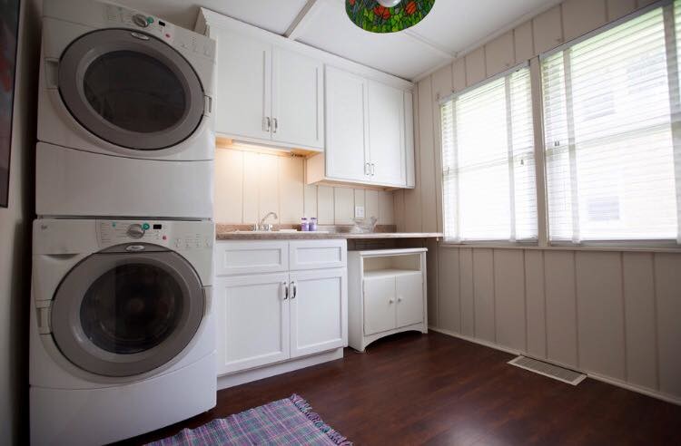 Immagine di una sala lavanderia stile marino di medie dimensioni con ante in stile shaker, ante bianche, pareti beige, parquet scuro e lavatrice e asciugatrice a colonna