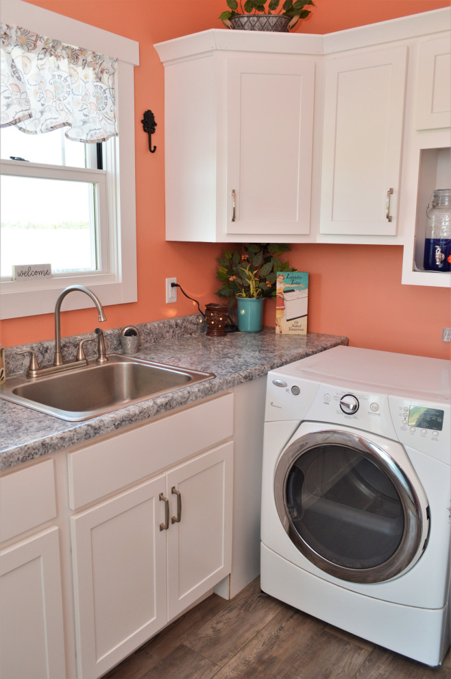 Inspiration för mellanstora lantliga l-formade grått tvättstugor enbart för tvätt, med en nedsänkt diskho, skåp i shakerstil, vita skåp, laminatbänkskiva, rosa väggar, laminatgolv, en tvättmaskin och torktumlare bredvid varandra och brunt golv