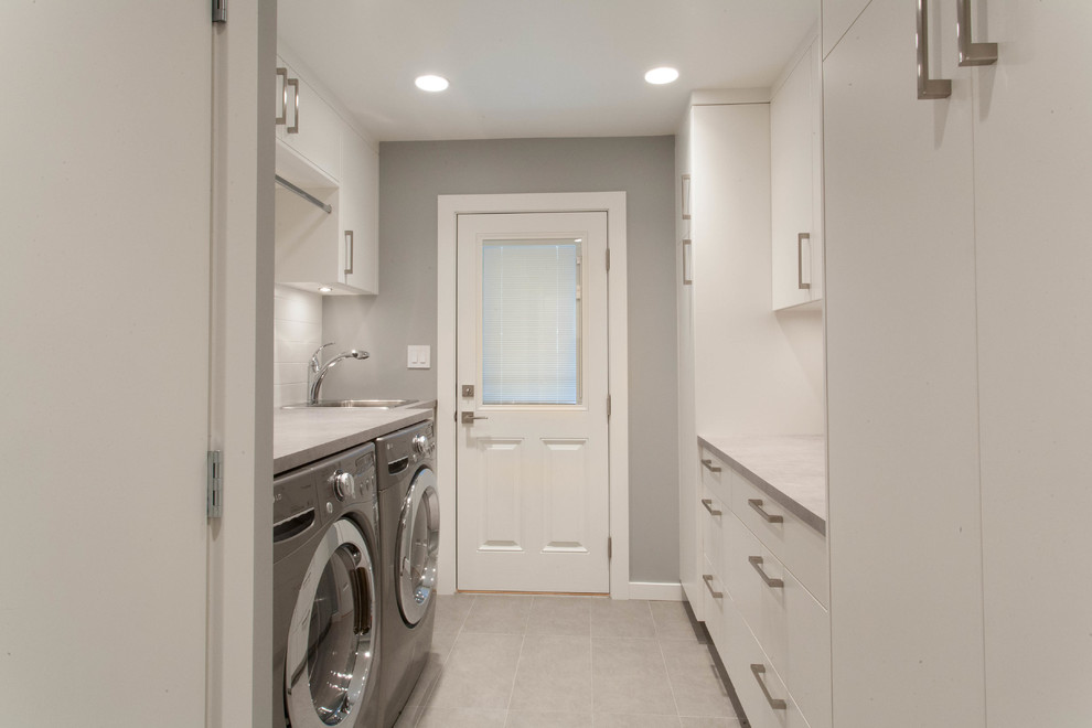 Zweizeilige, Mittelgroße Moderne Waschküche mit Einbauwaschbecken, flächenbündigen Schrankfronten, weißen Schränken, Laminat-Arbeitsplatte, grauer Wandfarbe, Keramikboden und Waschmaschine und Trockner nebeneinander in Vancouver