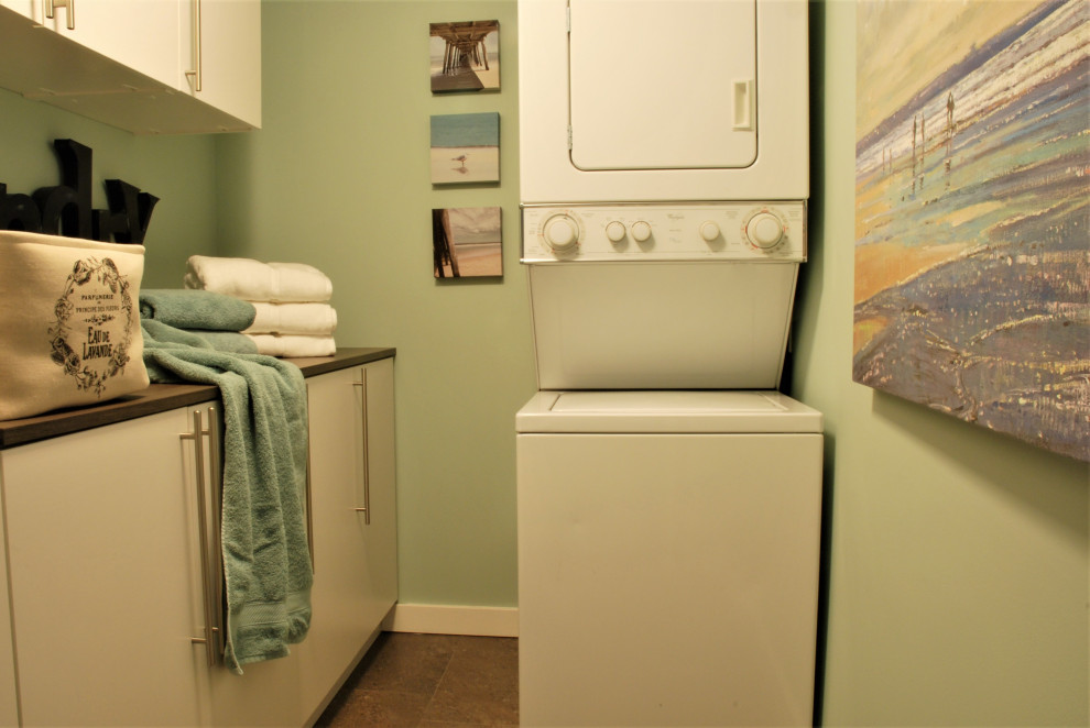 Klassisk inredning av en liten parallell tvättstuga enbart för tvätt, med släta luckor, gröna väggar, klinkergolv i porslin, en tvättpelare och brunt golv